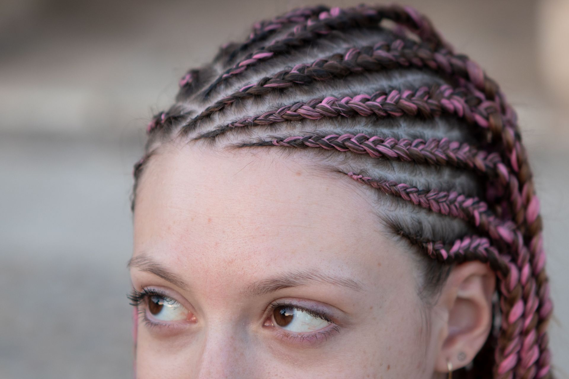 Detailed view of a woman featuring intricate pink and brown braided hairstyle, highlighting modern fashion.