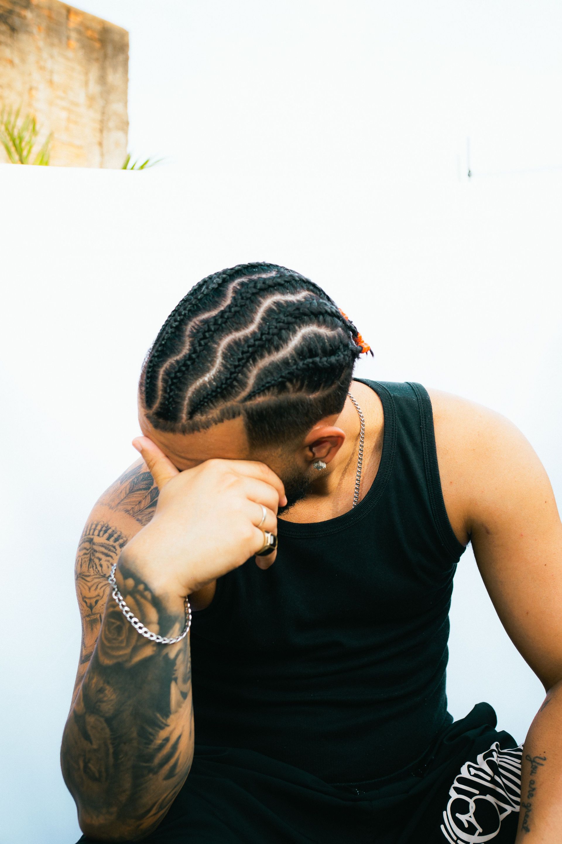 Tattooed man with intricate braids posing against a white background in São Paulo, Brazil.