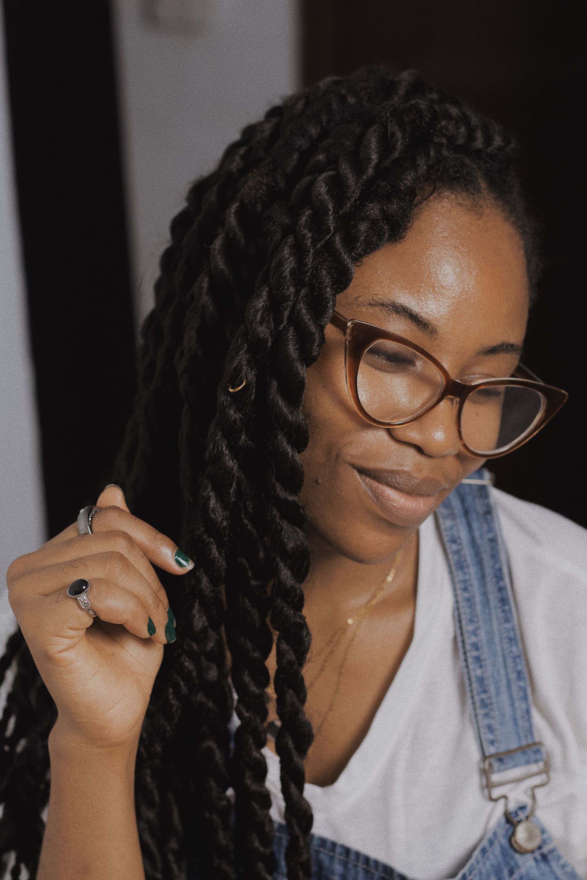 A smiling woman with dreadlocks and eyewear wearing a denim jumper.