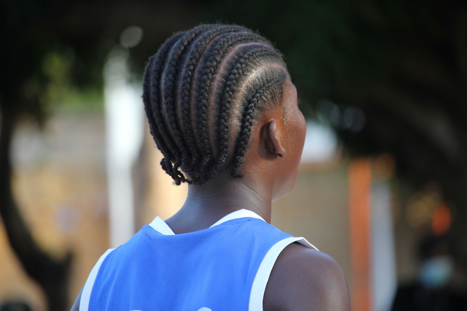 Back view of a person with cornrow braids in a blue jersey outdoors during the day.